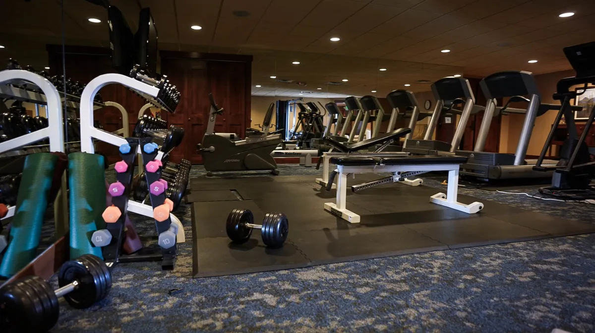A well-equipped fitness room featuring various gym equipment, including dumbbells, treadmills, and exercise benches. The space is bright and motivating, geared toward both solo workouts and group fitness activities.