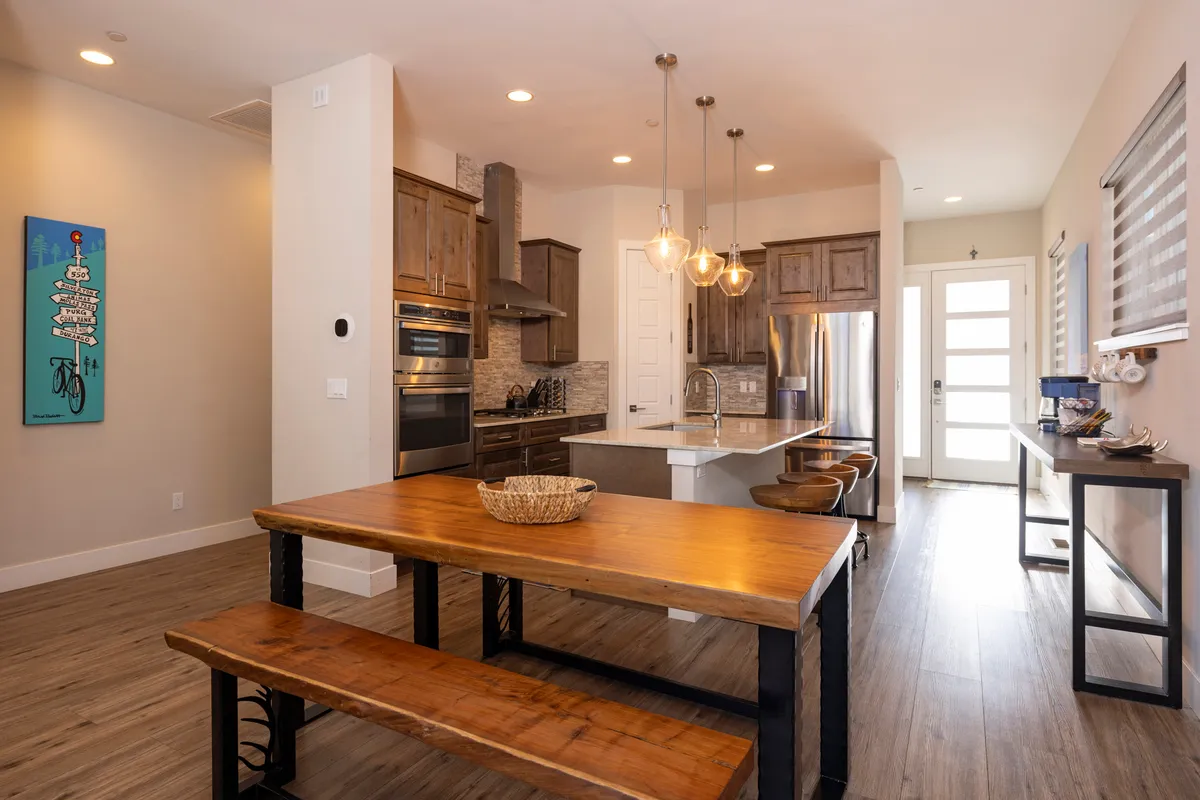 A large wooden dining table set beside a modern kitchen island, with ample light and tasteful artwork, showcasing a space designed for lively family gatherings and shared meals.