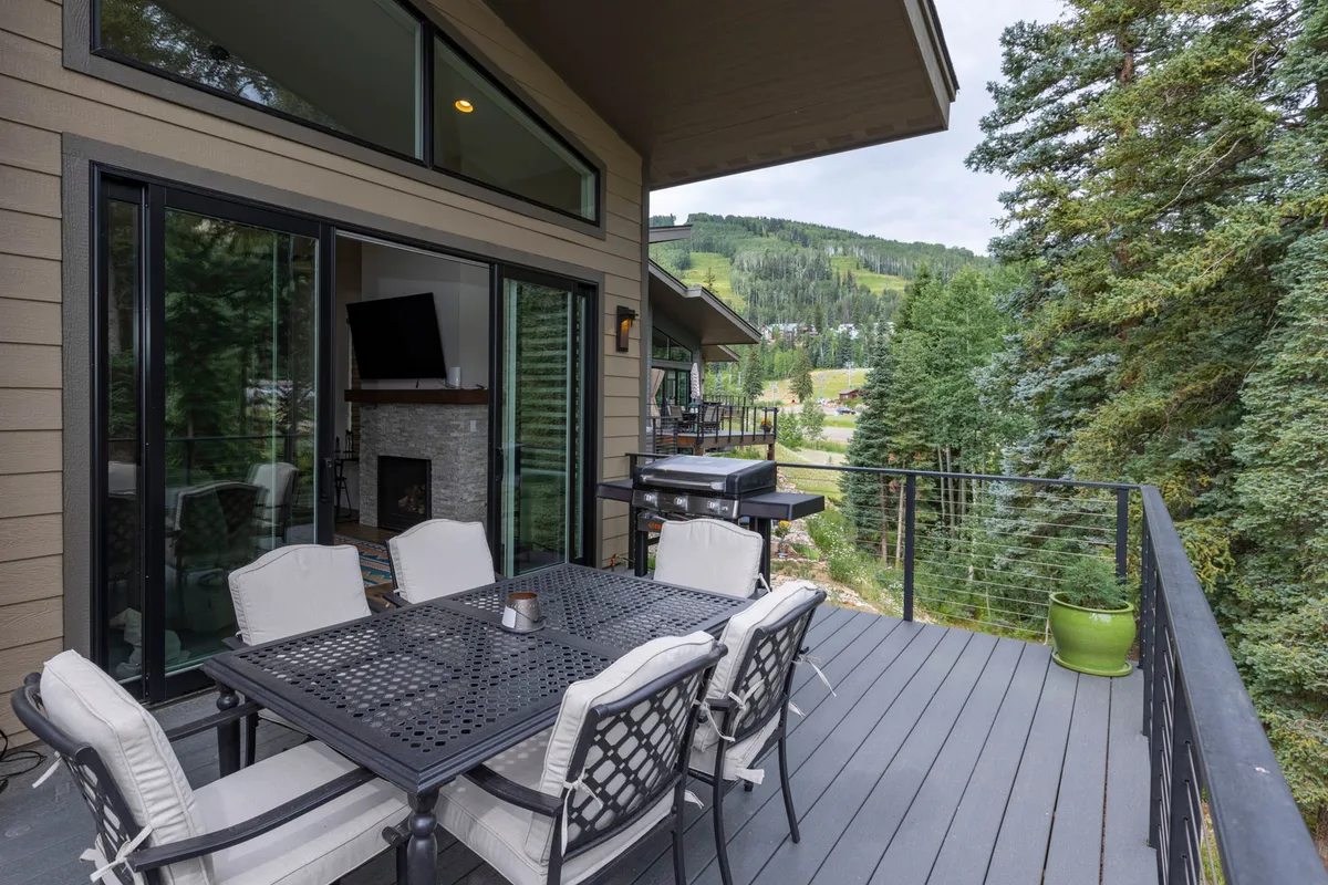 This image shows an inviting outdoor dining area with a dining table and grill set on a private patio or balcony. The scene features a spectacular mountain view through sliding glass doors, emphasizing a seamless connection between indoor and outdoor living spaces.