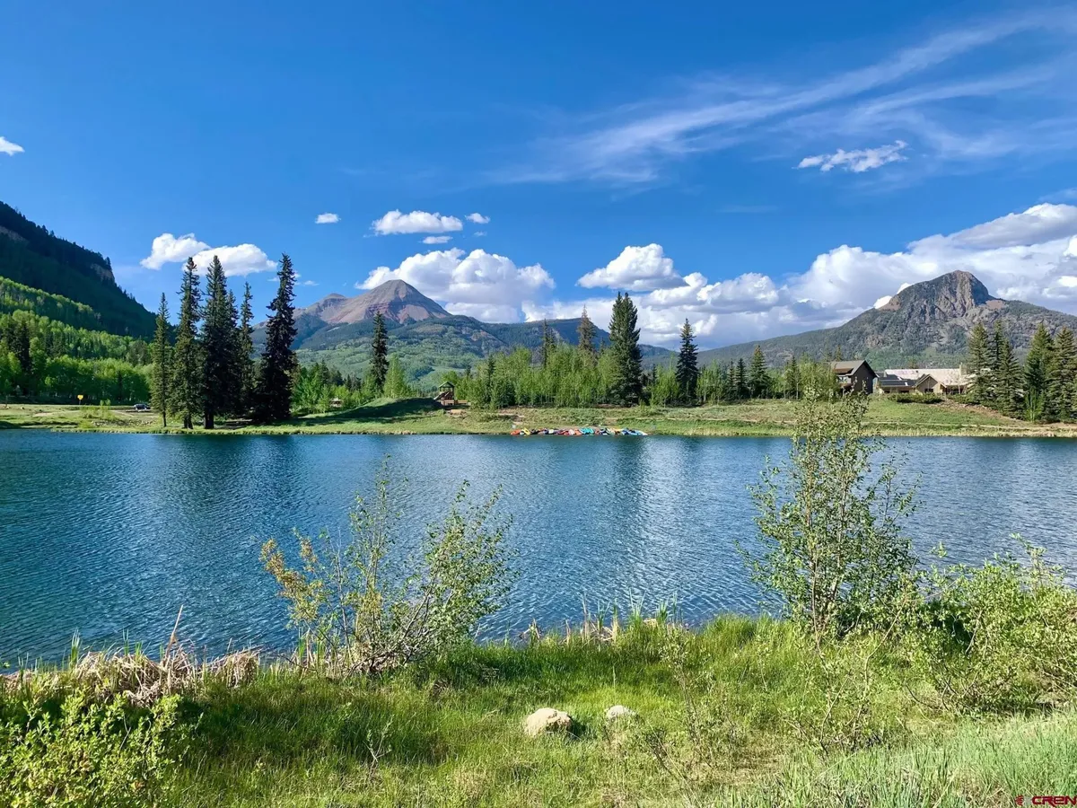 A serene panorama of a calm lake bordered by pine trees and distant mountains under a clear blue sky. The setting conveys peace and the opportunity for outdoor exploration, fishing, and connecting with nature.