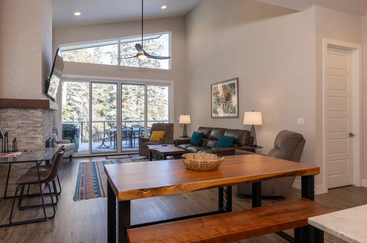 This image focuses on the dining area and adjoining living space, with large windows offering sunset-lit mountain views, comfortable seating, and tasteful wall art. The setup suggests intimate dinners and relaxed gatherings, underlining the versatility of the space.
